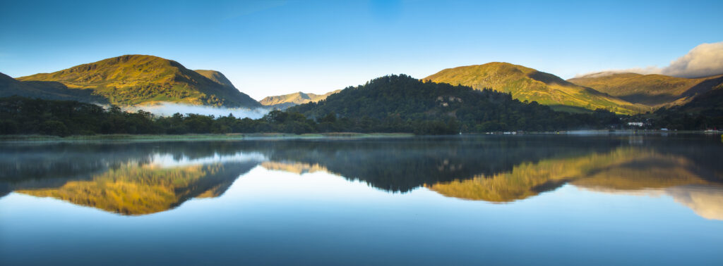 England, Cumbria, Lake District National Park. Helvellyn and surrounding mountain range reflected in still waters of Ullswater near Glenridding in Patterdale.
