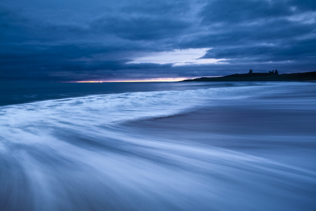 England Northumberland Embleton Bay. Dawn over the wild coastline of Embleton Bay overlooked by Dunstanburgh Castle