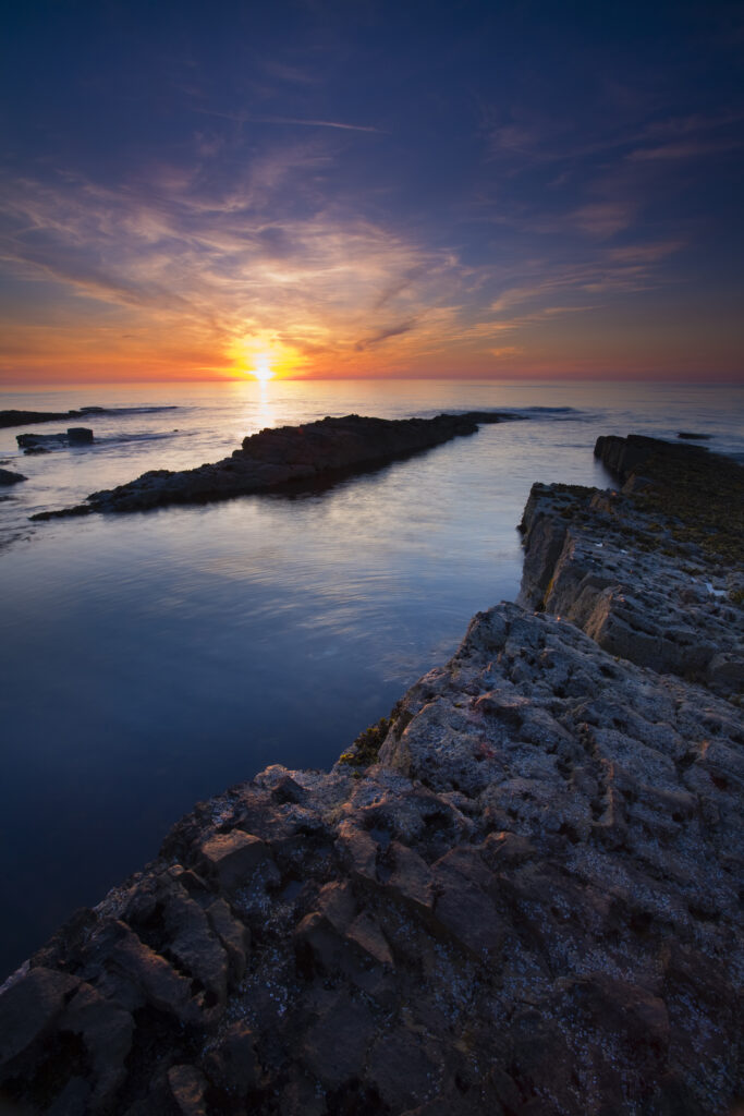 England, Northumberland, Beadnell. Sunrise over the North Sea viewed from Nacker Hole, Beadnell, situated along the Northumberland Heritage Coast.