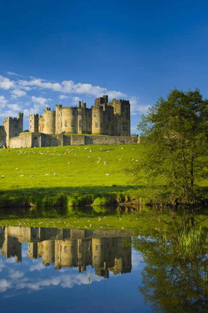 England, Northumberland, Alnwick. Alnwick Castle reflected in the still waters of the River Aln.