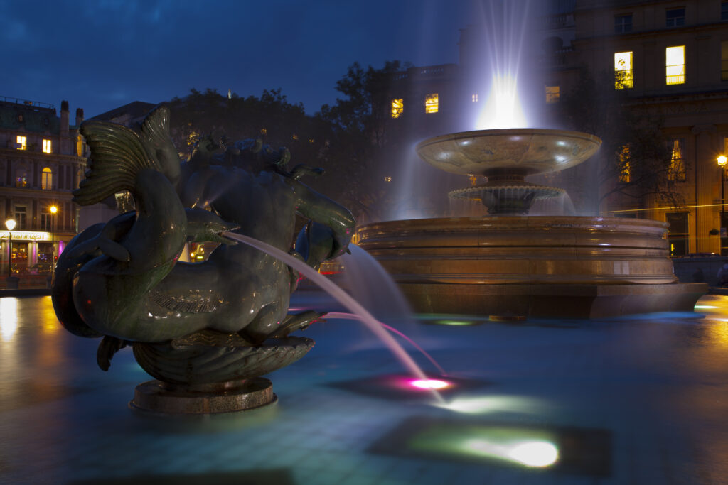 England, Greater London, City of Westminster. Flood lit fountains in Trafalgar Square, a popular tourist destination in London, photographed at dusk.
