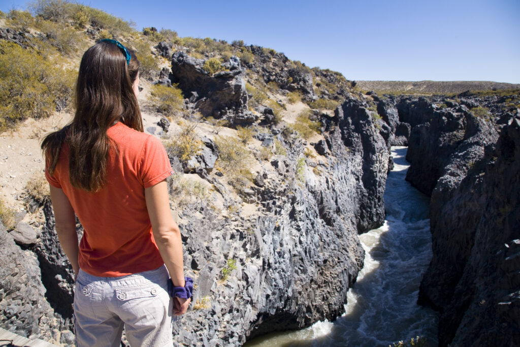 RF - Argentina, Mendoza, Parque Provincial Payunia. Female looking at a river flowing through a gorge.