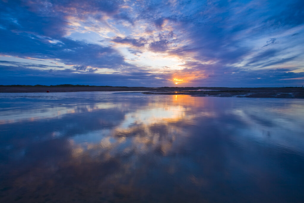 England, Cumbria, Lake District National Park. Clearing storm clouds at sunset, reflected in the still waters of the coastal town of Ravenglass.