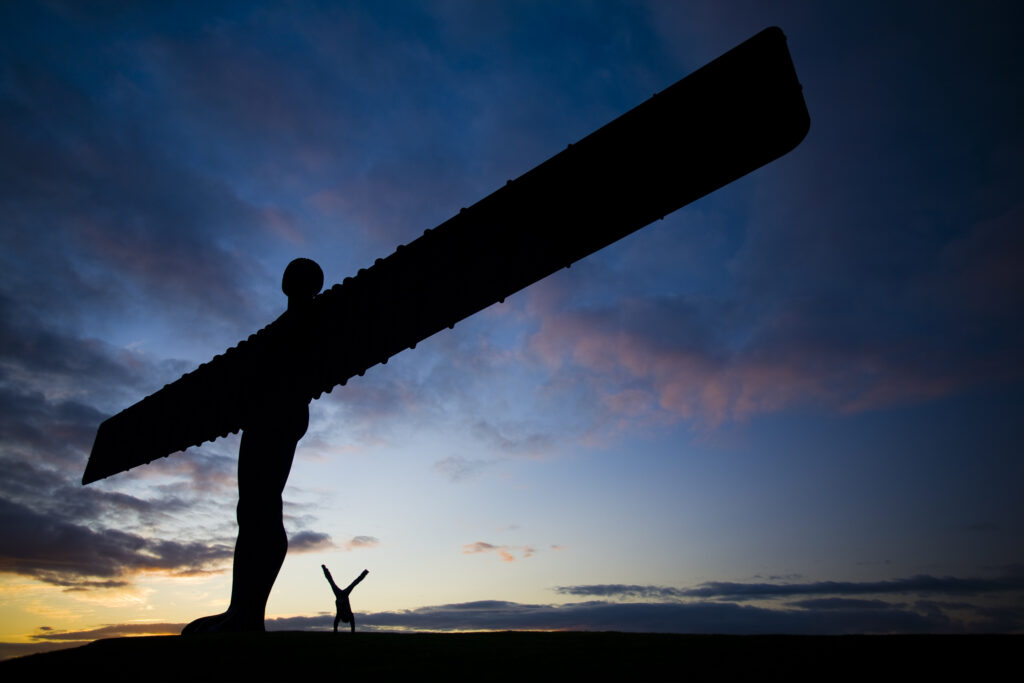 England, Tyne and Wear, Gateshead. Female performing a hand stand underneath the iconic Angel of the North.