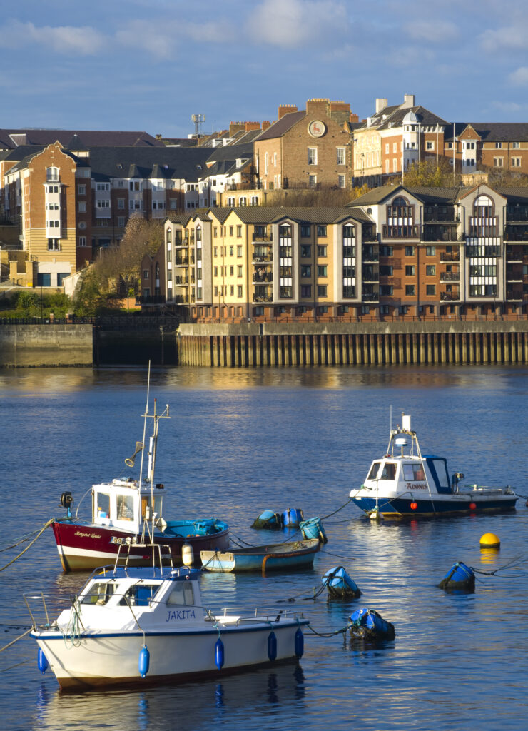 England, Tyne & Wear, North Shields. Boats moored on the River Tyne with a complex of new apartments located on the North Shields Quayside in the distance.