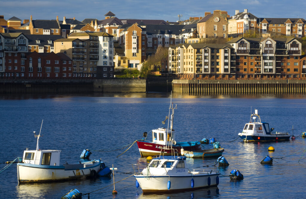 England, Tyne & Wear, North Shields. Boats moored on the River Tyne with a complex of new apartments located on the North Shields Quayside in the distance.