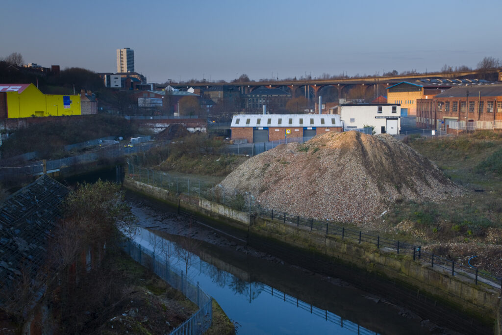 England, Tyne and Wear, Newcastle Upon Tyne. The Ouseburn running through a disappearing industrial landscape. The 800 metre long Byker Viaduct can be seen in the distance.