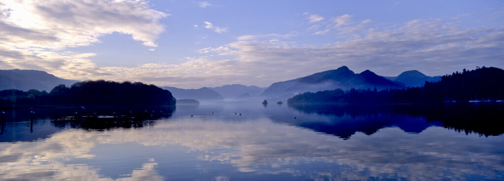 ENGLAND, Cumbria, Lake District National Park. Mountain backdrop reflected in the still waters of Derwentwater at dawn.