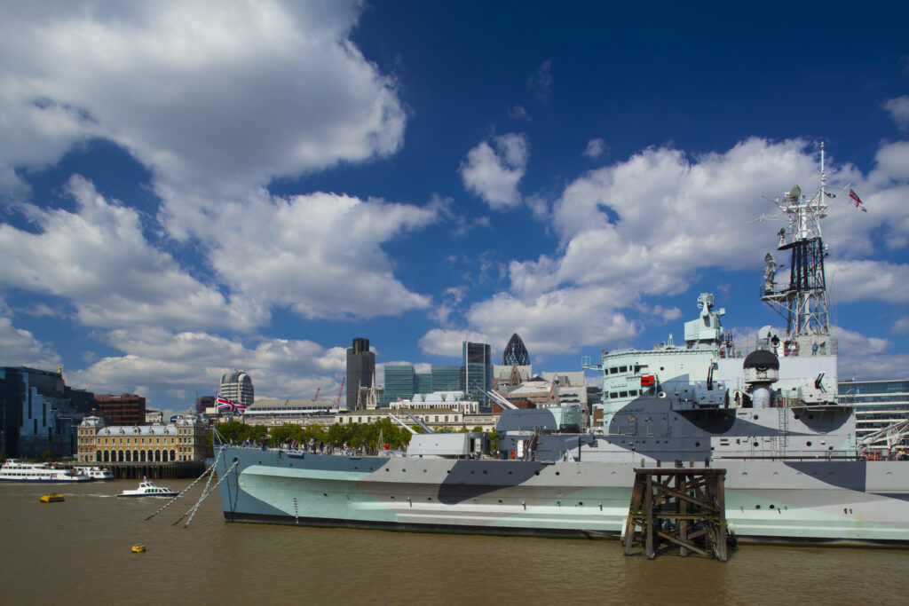 England, London, Southwark. HMS Belfast, originally a Royal Navy light cruiser, permanently moored in London on the River Thames with the City of London and the Gherkin in the distance.