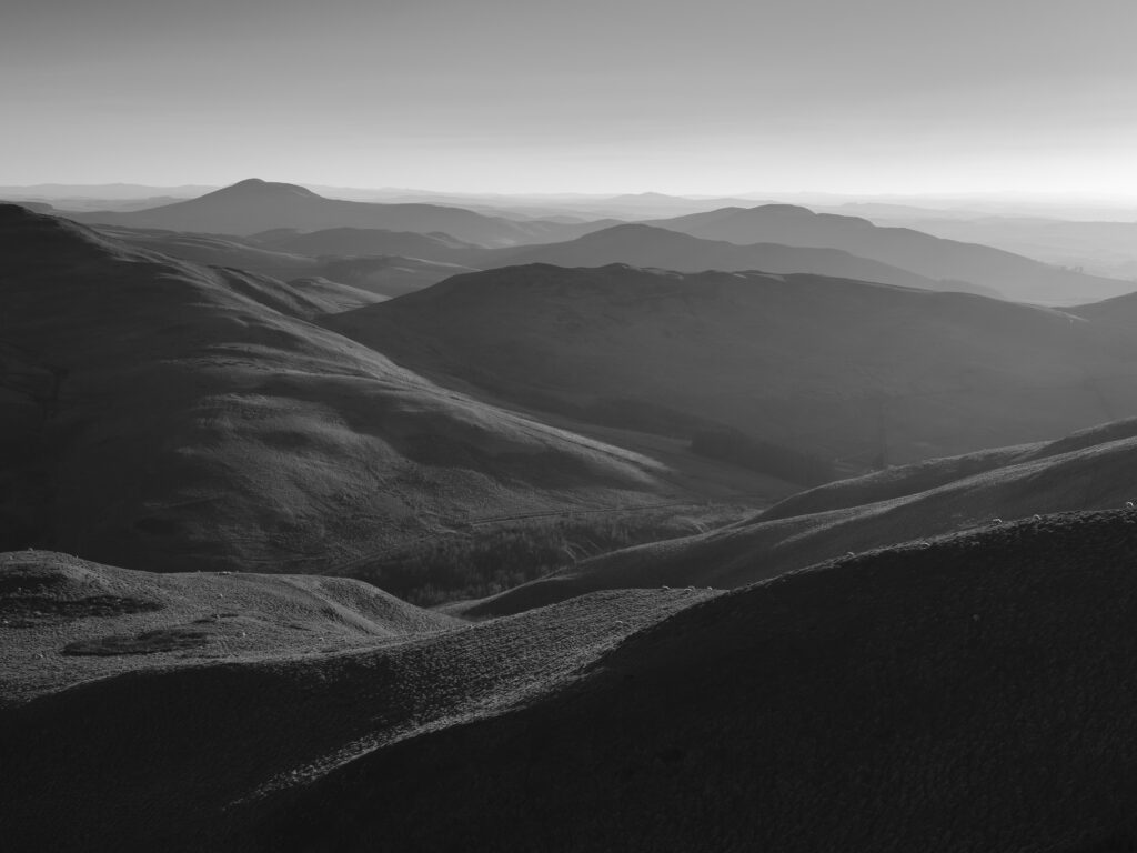 Scotland, Scottish Borders, Kirk Yetholm. View from the Pennine Way near White Law in Northumberland, looking towards Wildgoose Hill, Latchly Hill, the Southern Uplands and the Eildon Hills in the Scottish Borders, on a misty evening at sunset.